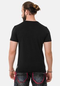 Schwarzes Kurzarm-T-Shirt mit Rundhalsausschnitt, glatter Textur und kleinem Logo nahe dem Saum, getragen mit grauen Cargo-Hosen mit pinken Akzenten.