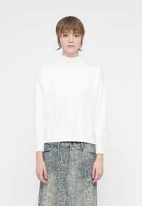 Sweater branco de gola alta canelado com ombros caídos, combinado com uma saia de ganga cinza, estampada, com um design de pele de cobra.