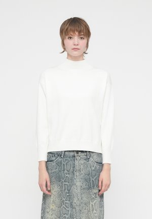 Hvit ribbestrikket turtleneck genser med senkede skuldre, kombinert med en grå, mønstret denimskjørt med slangeskinn-design.