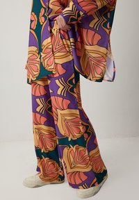 Két darabból álló szett, amely tartalmaz egy felsőt és bő szárú nadrágot élénk lila, narancs és arany virágmintákkal. Könnyű anyagból készült.