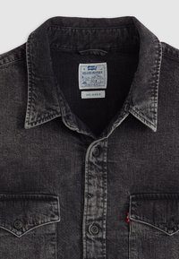 Camisa vaquera de denim negro con cierre de botones en la parte delantera, cuello puntiagudo, dos bolsillos en el pecho y un corte relajado. Etiqueta de Levi's visible en el interior.