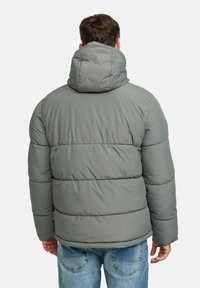 Homme portant une veste grise rembourrée avec capuche, vu de dos, associée à un jean en denim bleu.