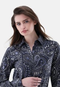 Camicia a maniche lunghe di un blu navy scuro con un intricato motivo paisley bianco e azzurro chiaro, dotata di colletto a punte e chiusura con bottoni.