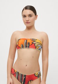 Bikini set bez ramienok v oranžovej a červenej farbe s abstraktnými vzormi. Obsahuje bezšvové okraje a kontrastné dekoratívne stehy.