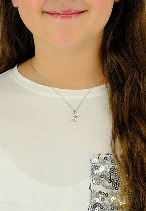 Collier avec pendentif éléphant en argent sur une fine chaîne, porté sur une chemise blanche avec un détail de poche à sequins en argent et noir.