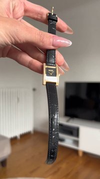 Black leather watch strap with a rectangular gold-tone case and black dial. Features five gold dots and a gold hour hand.