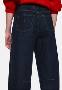 Dunkelblaue Jeans aus Denim mit sichtbaren Gesäßtaschen, kontrastierenden Nähten und lockerem Sitz, die ein sauberes, klassisches Design präsentieren.