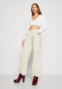 Beige cargo bukser med sidelommer, teksturert stoff og knappelukking, kombinert med glinsende bordeaux plattformhæler. Hvit ribbet crop-top.