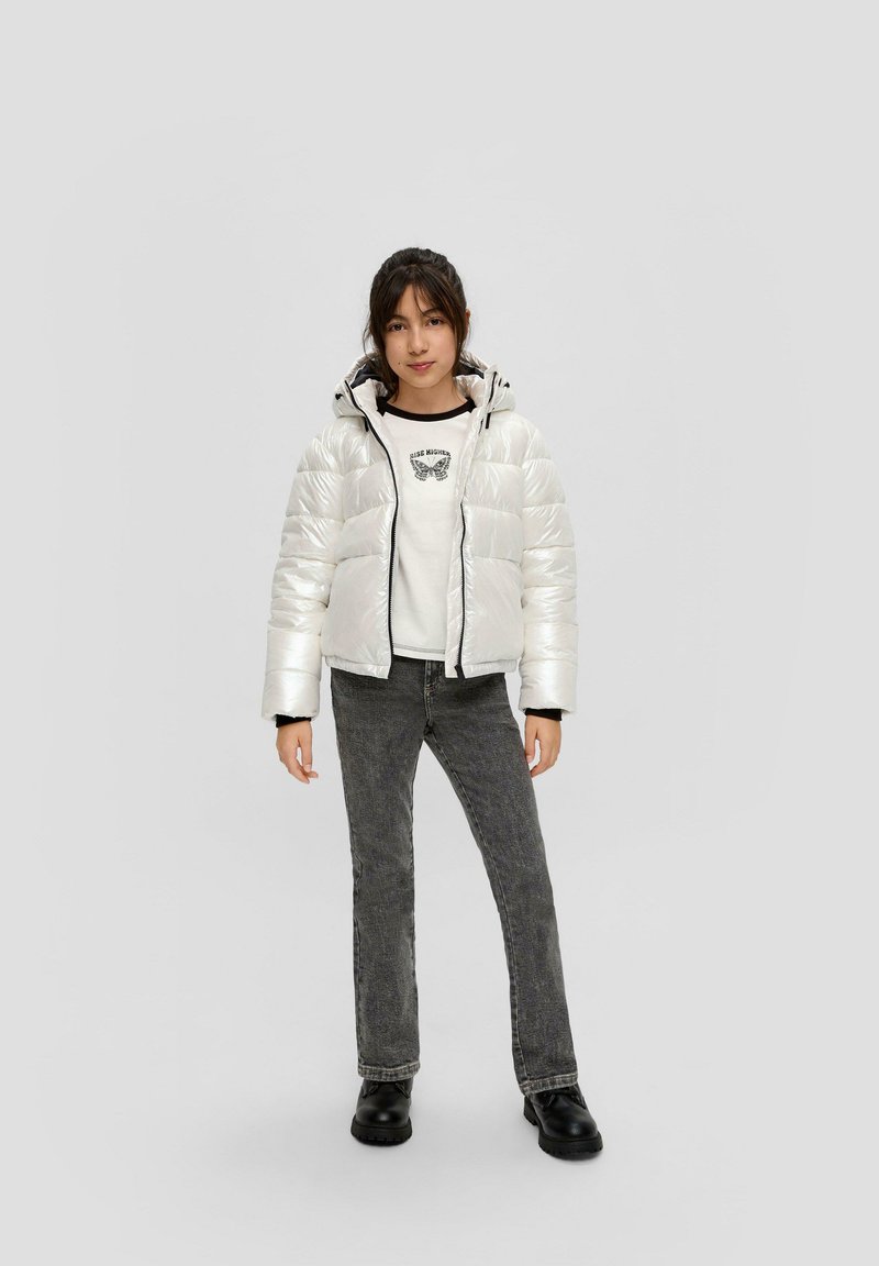 Weiße, dicke, isolierte Jacke mit Kapuze; schwarzer Reißverschluss und Akzente. Kombiniert mit einem grafischen weißen Sweatshirt und dunkelgrauen Jeans.