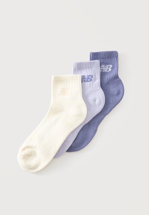 Trois chaussettes chevilles New Balance en crème, lavande clair et violet, disposées en chevauchement sur un fond blanc.