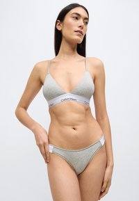 Γκρι βαμβακερό μπραλέτο με τριγωνικά cups και λεπτές τιράντες, με λογότυπο Calvin Klein στη ζώνη κάτω από το στήθος. Συνοδευτικό γκρι μπικίνι κάτω μέρος με λεπτομέρειες λογότυπου.