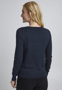 Marinblå stickad tröja med rund hals, långa ärmar och ribbad mudd. Slät textur med en något kroppsnära design.
