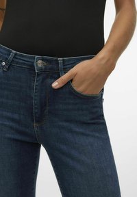 Jeans in denim blu scuro con un design aderente, dotati di una tasca frontale, chiusura con bottone metallico e una leggera texture di sbiadimento per i dettagli.