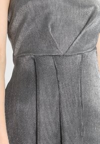 Robe plissée gris métallisé en tissu texturé, avec un décolleté en V et un corsage ajusté qui se prolonge en une jupe fluide.