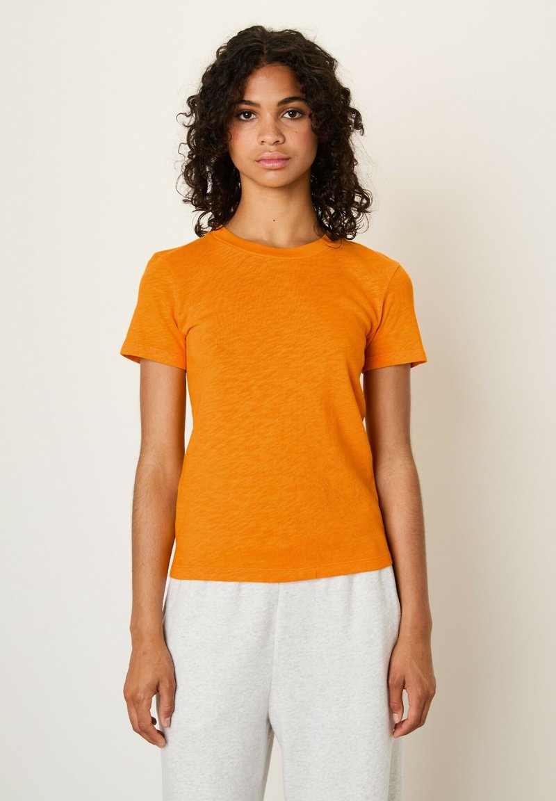 Oranje T-shirt met korte mouwen en een ronde halslijn, met een gladde textuur en een getailleerd ontwerp, gecombineerd met grijze trainingsbroek.
