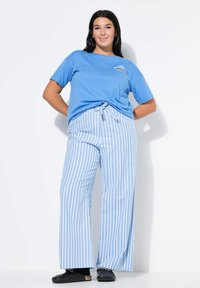 Modré bavlněné tričko s nápisem „DREAM“, kombinované se světle modrými širokými kalhotami s bílými pruhy a černými dřeváky.