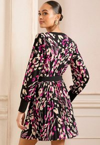 Crna haljina s šarenim apstraktnim uzorkom u ružičastoj, krem i lavandi. Dugi napuhani rukavi i plisirana suknja s crnim pojasom.