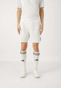 Weiße Fußballshorts und Socken mit drei schwarzen Streifen oben, getragen mit hellen Fußballschuhen. Einfaches Design, Sportmaterial.