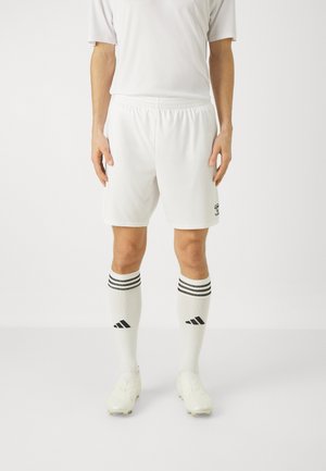 Witte voetbalshorts en sokken met drie zwarte strepen aan de bovenkant, gedragen met lichtgekleurde voetbalschoenen. Eenvoudig ontwerp, sportkledingmateriaal.