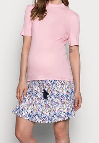Světle růžové žebrované tričko a krátká sukně s barevným vzorem, která má abstraktní designy a černý třásňový detail v pase.