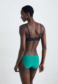 Sutiã preto com alças ajustáveis e fecho de gancho, combinado com roupa interior teal de cintura baixa. Tecido suave com detalhes mínimos.