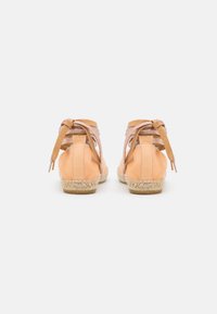 Sapatos espadrilles com parte superior em couro pêssego, sola de juta trançada e duas tiras de tecido atadas na parte de trás em um rosa metálico claro.