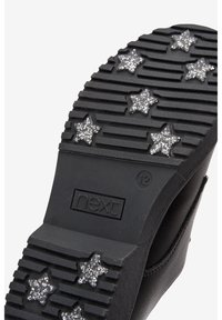 Semelle en caoutchouc noir avec des rainures texturées et sept accents étoilés en paillettes argentées, marquée "next" et taille "12". Conception durable et pratique.
