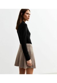 Haut noir à manches longues associé à une jupe patineuse en plaid dans des tons beige et marron, avec un design évasé et une texture plissée.