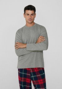 Šedé tričko s dlouhým rukávem z měkké látky, v kombinaci s károvanými pyžamovými kalhotami v červené, modré a zelené barvě. Jednoduchý kulatý výstřih.