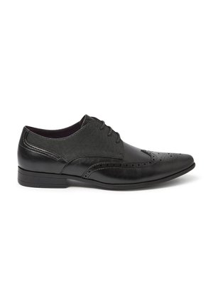 Chaussure habillée pour homme en cuir noir avec perforations en forme d'aile, fermeture à lacets et panneaux latéraux en tissu texturé.
