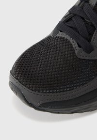 Svart sportssko med mesh-overdel og teksturert overflate, med rund tå, forsterkede sider og forsterket søm.