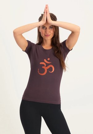 Dunkelviolettes Baumwoll-T-Shirt mit einem großen orangen Om-Symbol in der Mitte der Vorderseite. Taillierter Schnitt mit kurzen Ärmeln und Rundhalsausschnitt.