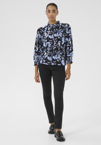 Blusa nera e blu con un motivo floreale, scollatura arricciata e maniche lunghe a sbuffo, abbinata a pantaloni neri slim-fit e mocassini lucidi.