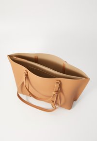 Smilga tan tote soma ar teksturētu apdari, atvērta augšdaļa, divi plecu siksniņas un iekšējā rāvējslēdzēja kabata. Iekļautas zelta toņa aksesuāri.