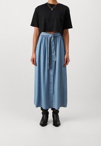 Svart kortärmad t-shirt och ljusblå denimkjol med knytning i midjan, med en knappslå framtill och flödande design. Svarta stövlar fulländar looken.