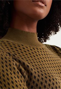 Knit sweater with a ribbed high neckline in olive green, featuring a textured pattern of black dots against a smooth background.