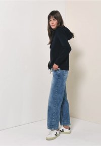 Sweatshirt à capuche navy avec poches avant, associé à un jean large en denim bleu clair et des baskets blanches avec des accents verts.
