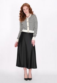 Zwart-wit gestreepte cardigan met knopen aan de voorkant, gecombineerd met een lange, zwarte satijnen rok. Hakken in zwart ronden de look af.