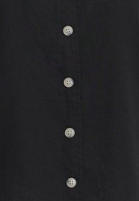 Tissu noir avec une rangée de cinq boutons ronds gris clair, espacés régulièrement, cousus verticalement au centre.