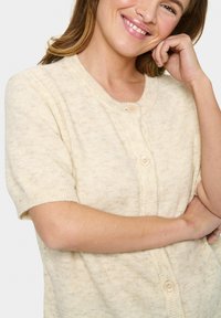 Világos bézs színű, rövid ujjú kardigán pulóver, puha, textúrált anyagból készült, kerek nyakkal és három gombos lezárással elöl.