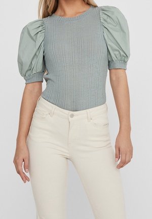 Lysegrøn ribstrikket bodystocking med puffede ærmer, kombineret med cremefarvede tætsiddende jeans. Glat tekstur og tætsiddende design.