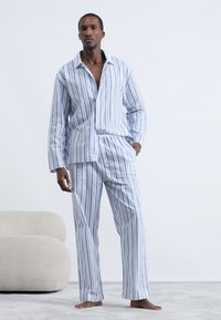 Set de pijama din bumbac cu dungi verticale albastre și albe, cămașă lejeră cu guler și închidere cu nasturi, pantaloni cu talie elastică.