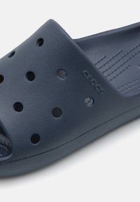 Sandal cu toc albastru închis, fabricat dintr-un material texturat și flexibil. Prezintă orificii de ventilație și numele mărcii embosat pe lateral.