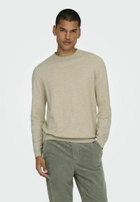 Licht beige trui met een ronde halslijn en lange mouwen, gemaakt van zachte stof. Gecombineerd met groene corduroy broeken, met zichtbare voorkruisjes.
