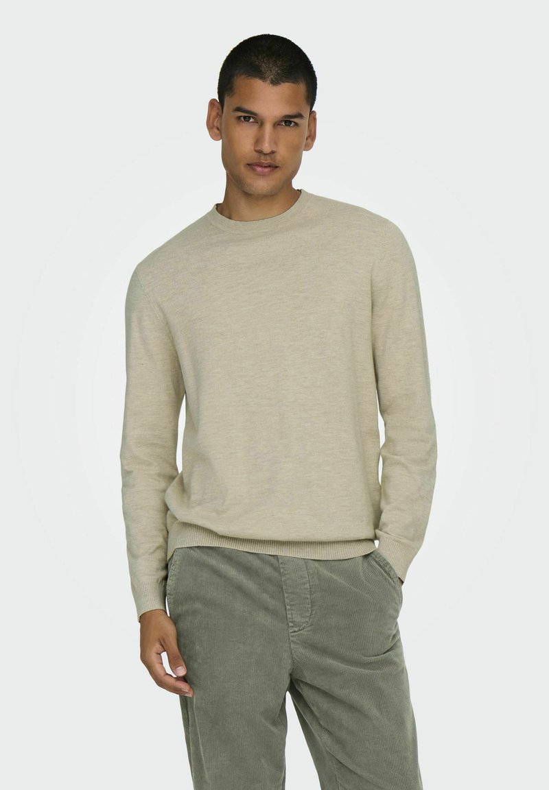 Licht beige trui met een ronde halslijn en lange mouwen, gemaakt van zachte stof. Gecombineerd met groene corduroy broeken, met zichtbare voorkruisjes.