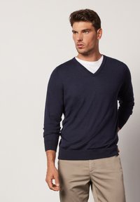 Navyblauer V-Ausschnitt-Pullover aus weichem Strickstoff mit langen Ärmeln und gerippten Bündchen. Kombiniert mit hellbeigen Hosen.