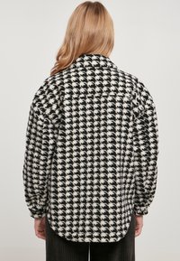 Sort-hvid hundetand mønsteret skjorte med en fluffy tekstur, oversized pasform og spids krave. Bagview, der viser den buede hank.