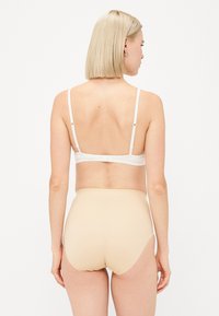 Lichtbeige hoge taille ondergoed van gladde stof, met volledige bedekking en dunne elastische bandjes. Eenvoudig ontwerp, zonder zichtbare patronen of accenten.