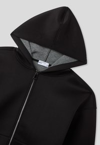 Felpa nera con zip e fodera grigia nel cappuccio, etichetta del marchio visibile e texture del tessuto liscia.