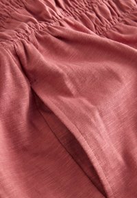 Tissu rose avec une texture douce, comportant un smocké froncé en haut et un matériau fluide avec un drapé décontracté.